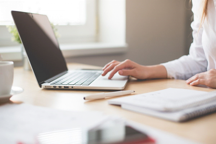 Title: Hands typing on a laptop at a bright desk with a notebook - Description: Hands typing on a laptop at a bright desk with a notebook