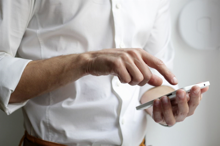 Title: Hands drafting a post on a smartphone above a laptop keyboard - Description: Hands drafting a post on a smartphone above a laptop keyboard