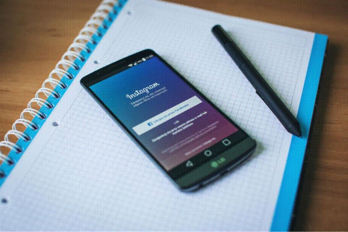 Title: Hand holding a smartphone showing an Instagram profile grid above a desk - Description: Hand holding a smartphone showing an Instagram profile grid above a desk