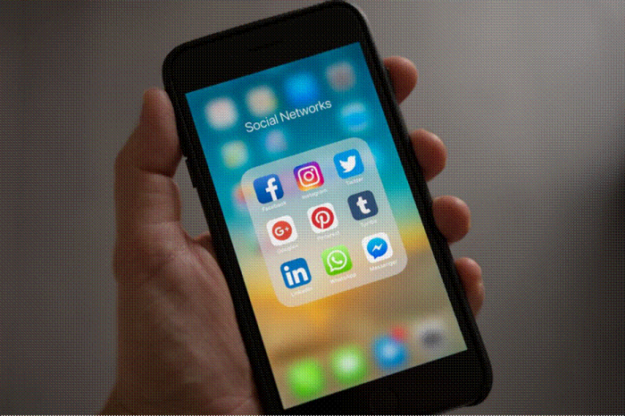 Title: Hand holding a smartphone with a folder of social media apps open - Description: Hand holding a smartphone with a folder of social media apps open
