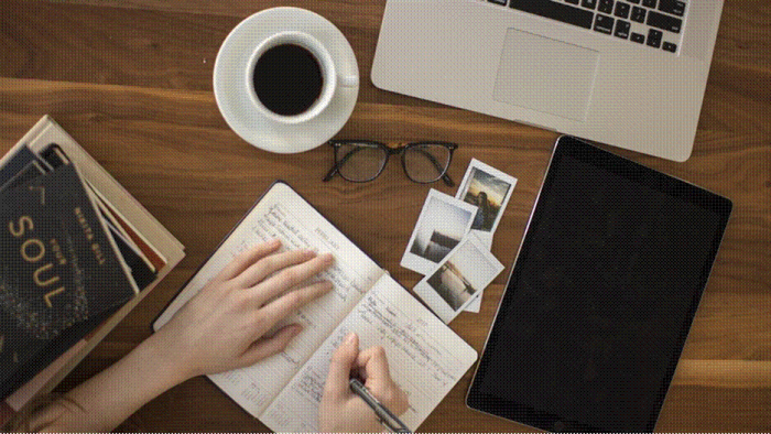Title: Hands drafting caption notes on paper next to a laptop, a tablet and a cup of coffee - Description: Hands drafting caption notes on paper next to a laptop, a tablet and a cup of coffee