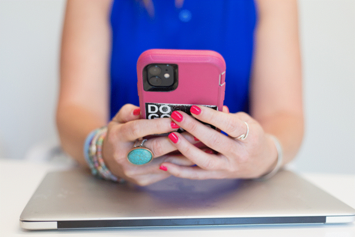 Title: Hands holding a smartphone above a laptop while checking X search results - Description: Hands holding a smartphone above a laptop while checking X search results