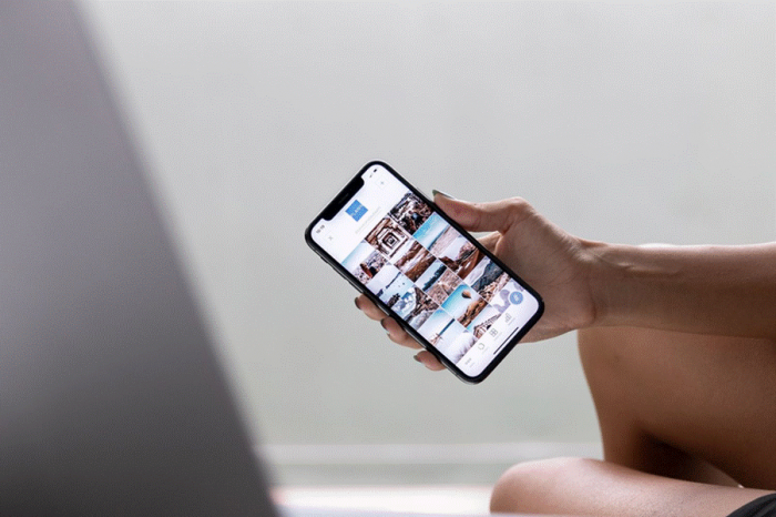Title: Person checking a profile on a phone screen next to a laptop - Description: Person checking a profile on a phone screen next to a laptop