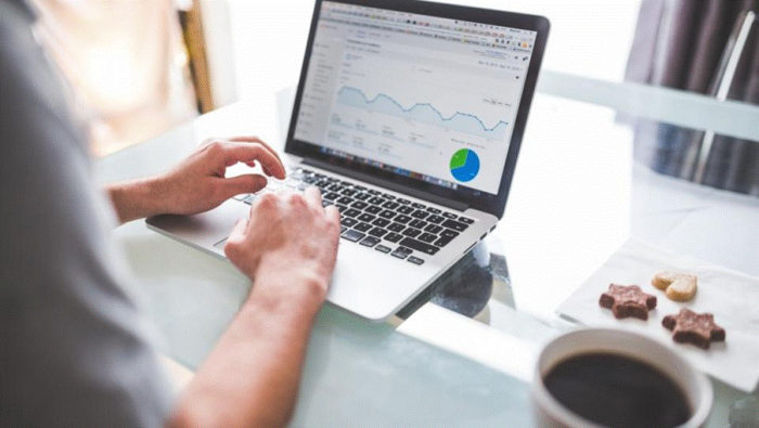 Title: Person working at a laptop that shows a website analytics dashboard, with coffee beside them - Description: Person working at a laptop that shows a website analytics dashboard, with coffee beside them